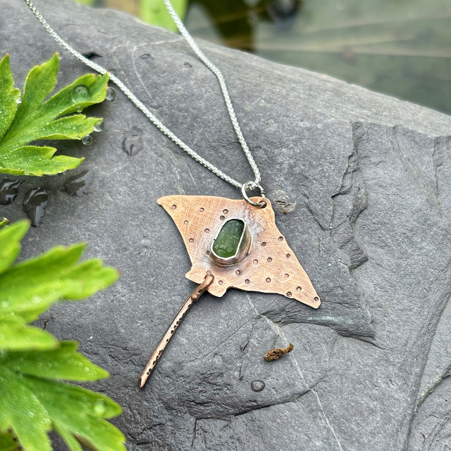 Necklace with a unique pendant on a stone surface with green leaves.