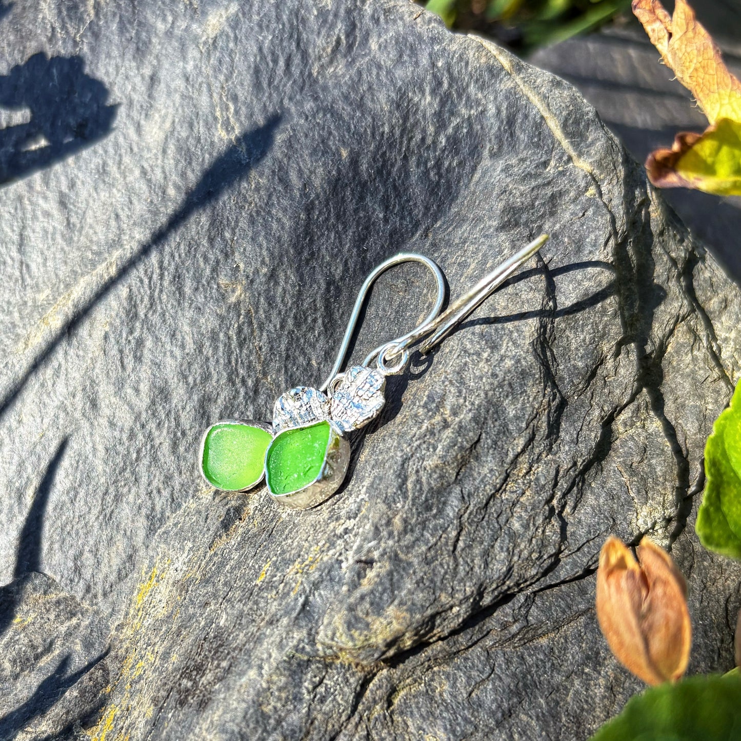 Silver earring with green leaves on a stone surface