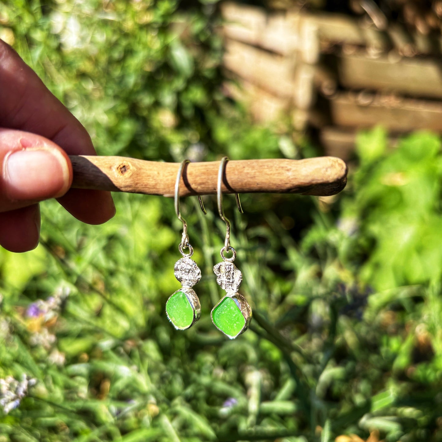 Green earrings hanging on a stick with a natural background
