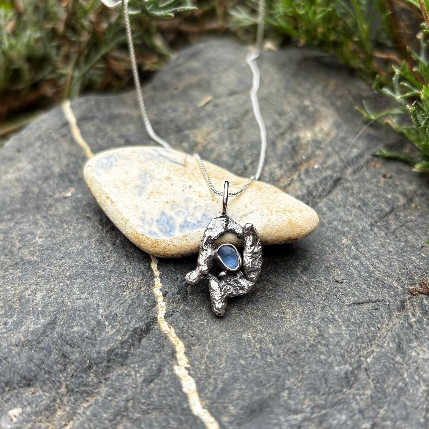 Silver pendant with a blue stone on a rocky surface
